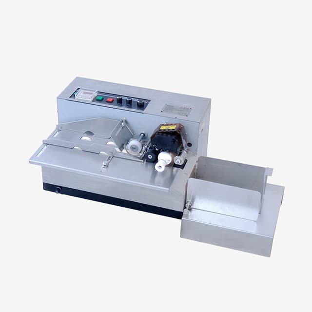 Real compact metal solid-ink coder on a neutral background with flat-item feeder, adjustable guides, print mechanism, controls and output tray. Reference equipment photograph.