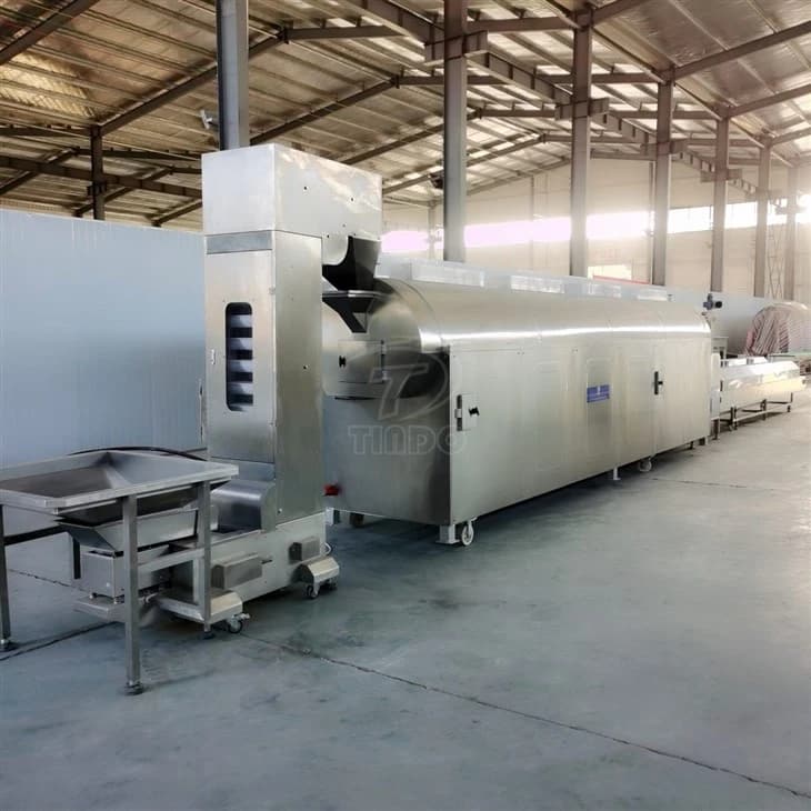 Tindo continuous nut roasting equipment photographed in a workshop, with an extended enclosed heating section. Reference equipment photograph.