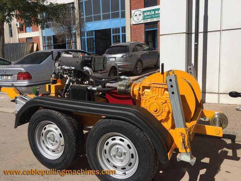 Yellow trailer-mounted cable capstan winch photographed outside a workshop. Reference equipment photograph.