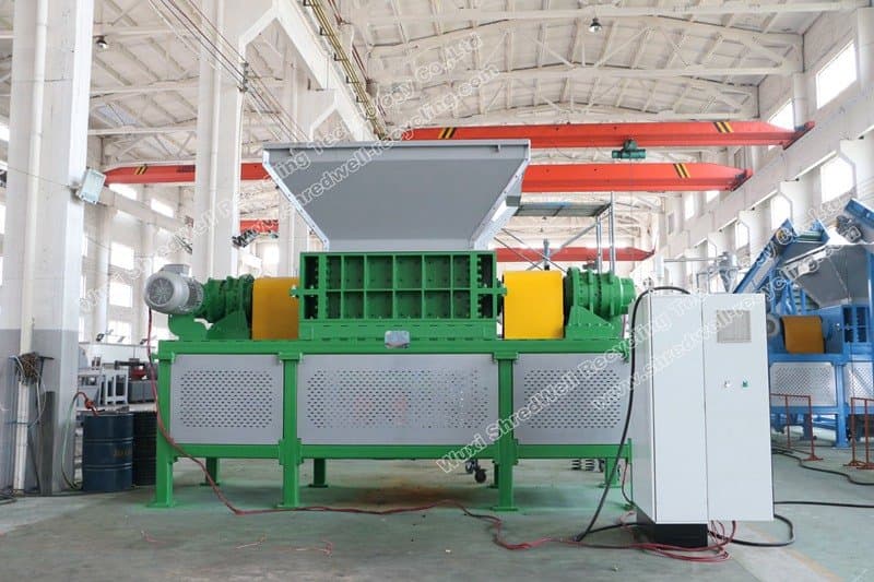 Shredwell tire shredder photographed in a workshop with its feed opening and guarded cutting body. Reference equipment photograph.