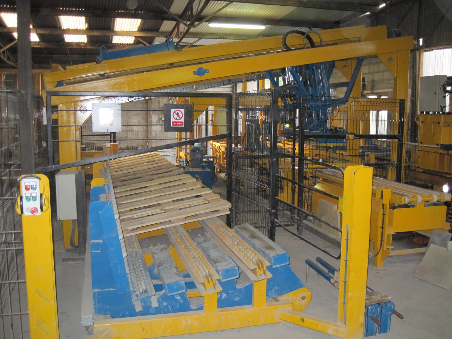 Installed yellow-and-blue production-line handling equipment in a workshop, showing conveyors, guarded transfer equipment and boards within the line. Reference equipment photograph.