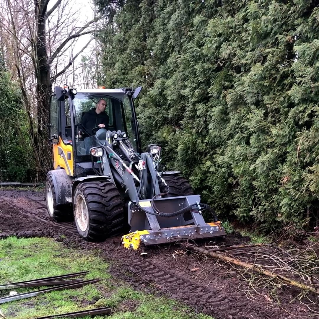 Giant forestry mulcher attached to a loader while working on woody vegetation. Reference equipment photograph.