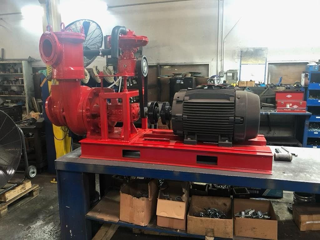 Red self-priming trash pump with black electric motor on a base, photographed in a workshop. Reference equipment photograph.