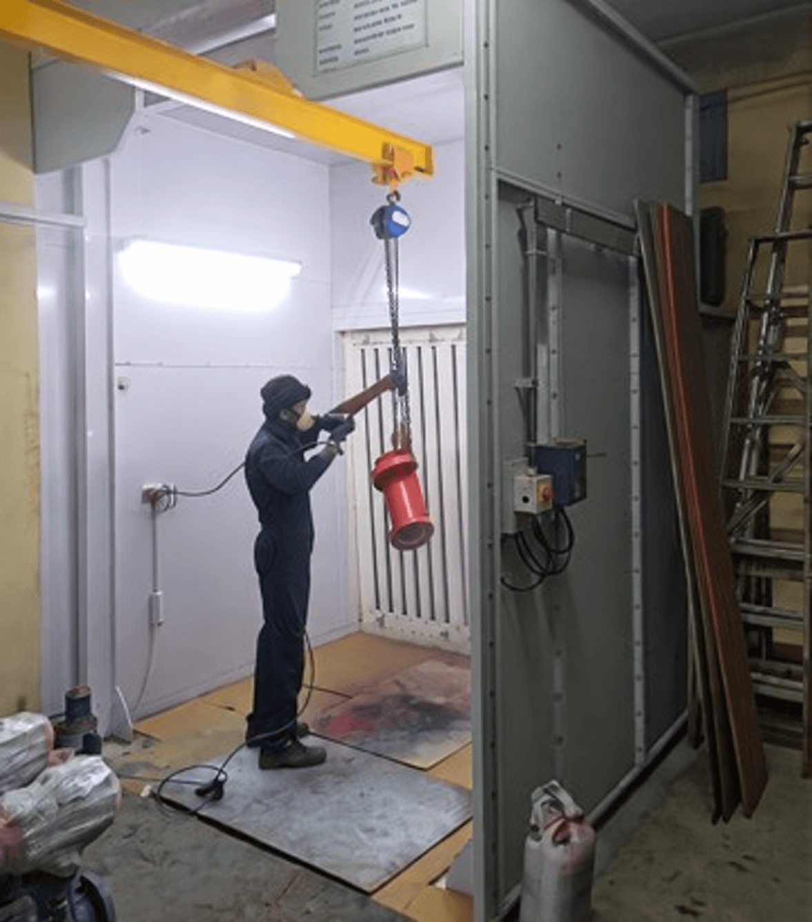 Industrial spray enclosure, extraction panel, hanging workpiece and operator; the promotional overlay was locally removed. Reference equipment photograph.