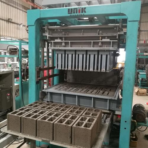 Actual green UNIK block-forming press in a workshop, with mould tooling and freshly formed hollow concrete blocks on an output pallet. Reference equipment photograph.