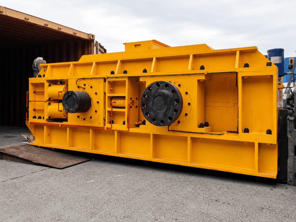 Yellow double-roll crusher photographed on shipping supports outside a workshop. Reference equipment photograph.