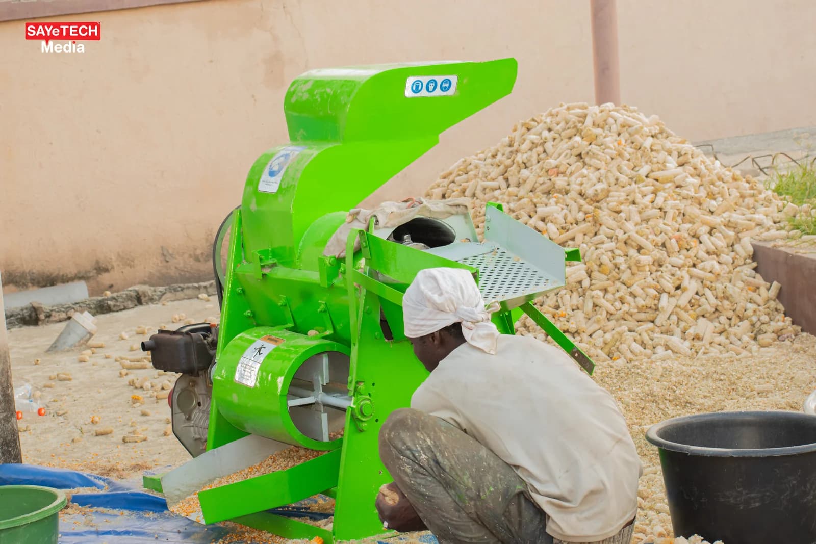 Green maize sheller being fed by an operator beside a pile of maize cobs. Reference equipment photograph.