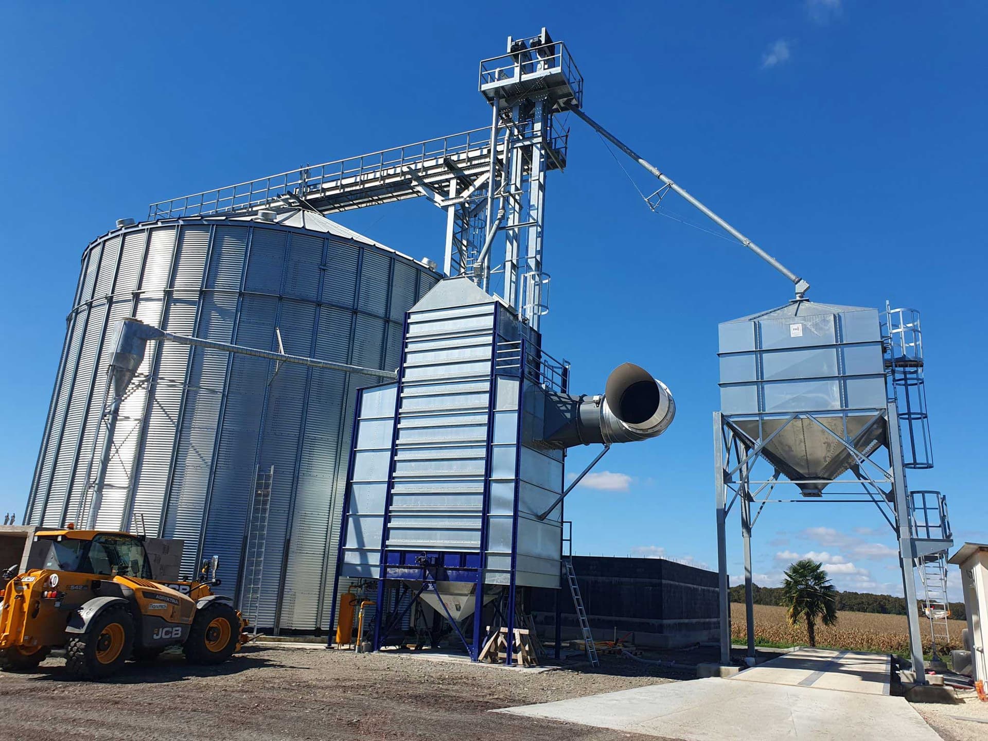 Installed outdoor grain dryer with vertical grain handling and an air duct. Reference equipment photograph.