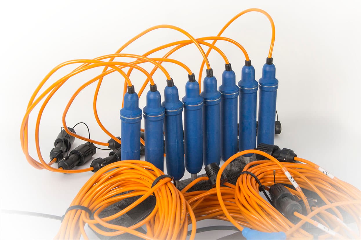 Blue geophone sensors interconnected by orange survey cables. Reference equipment photograph.