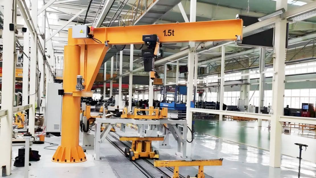 Column-mounted jib crane with a hoist in a factory work area. Reference equipment photograph.