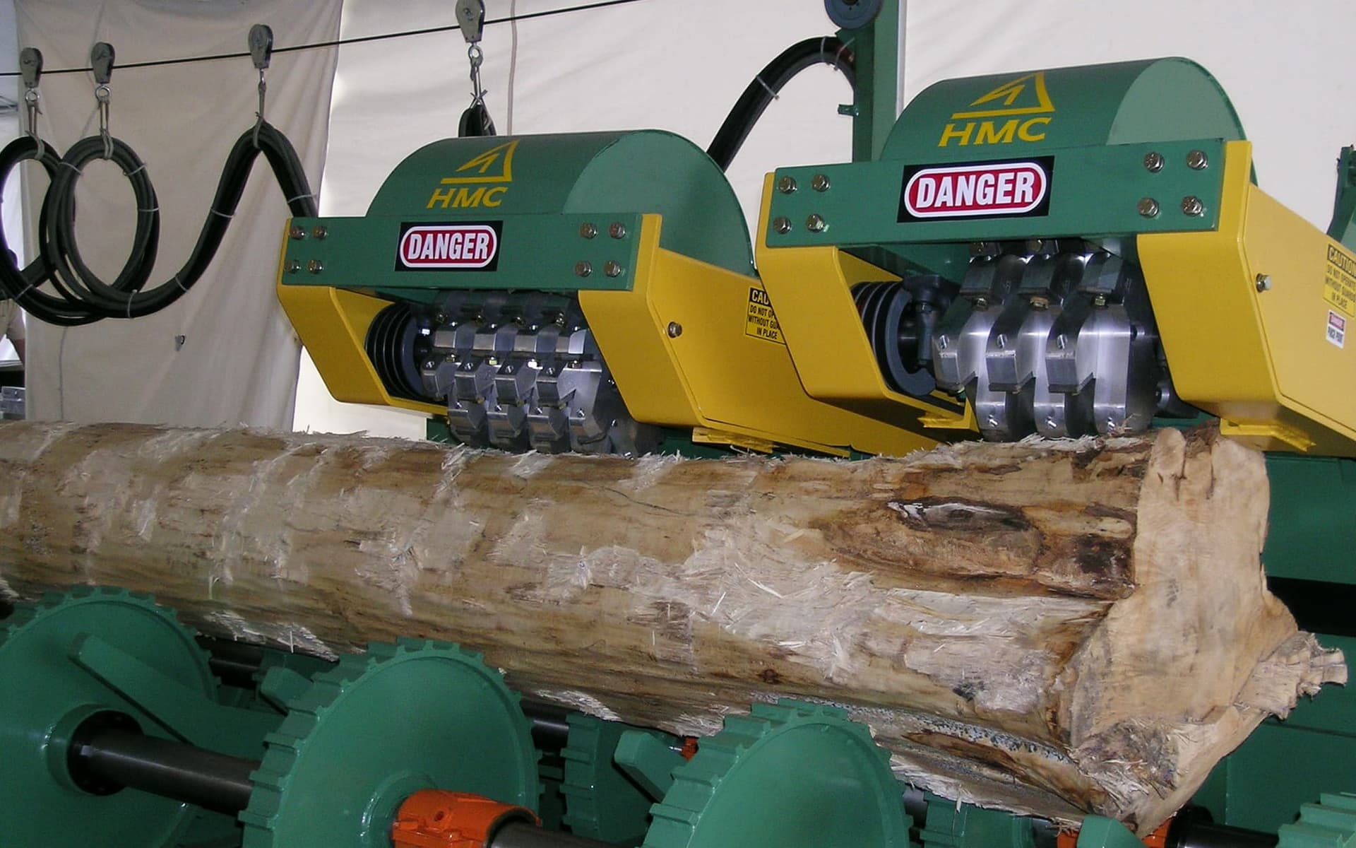HMC log debarker working on a log supported by powered rollers. Reference equipment photograph.