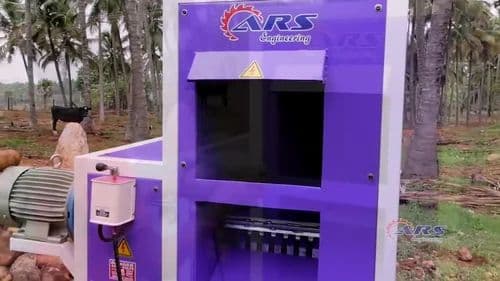 ARS coconut dehusking machine photographed outdoors with its purple housing and coconut feed opening. Reference equipment photograph.
